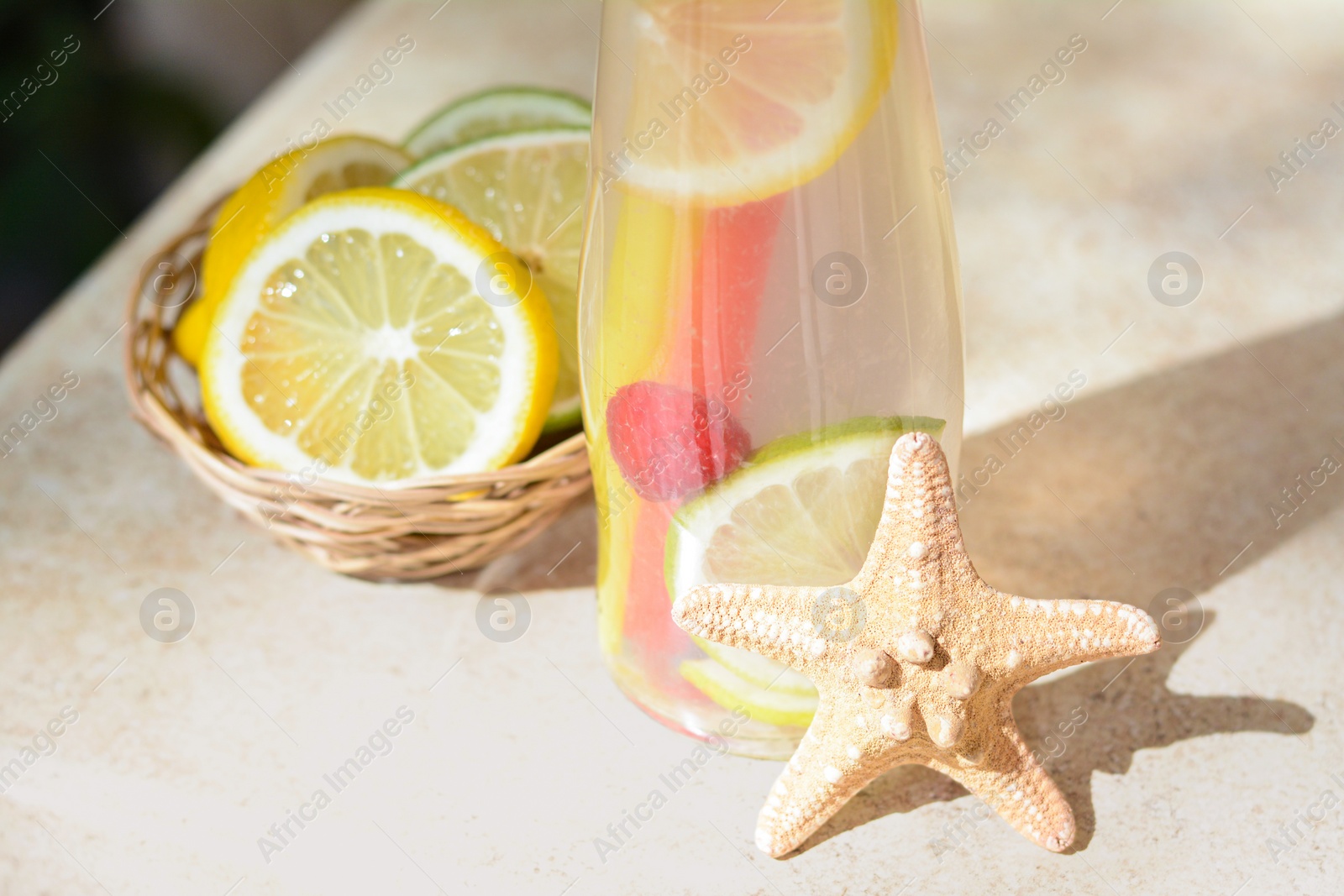 Photo of Citrus fruits and refreshing tasty lemonade served in glass bottle on beige table