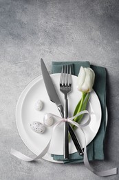 Photo of Festive table setting with painted eggs and white tulip on light grey background, top view. Easter celebration