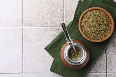 Photo of Calabash with bombilla, bowl of mate tea leaves and cloth on tiled surface, flat lay. Space for text
