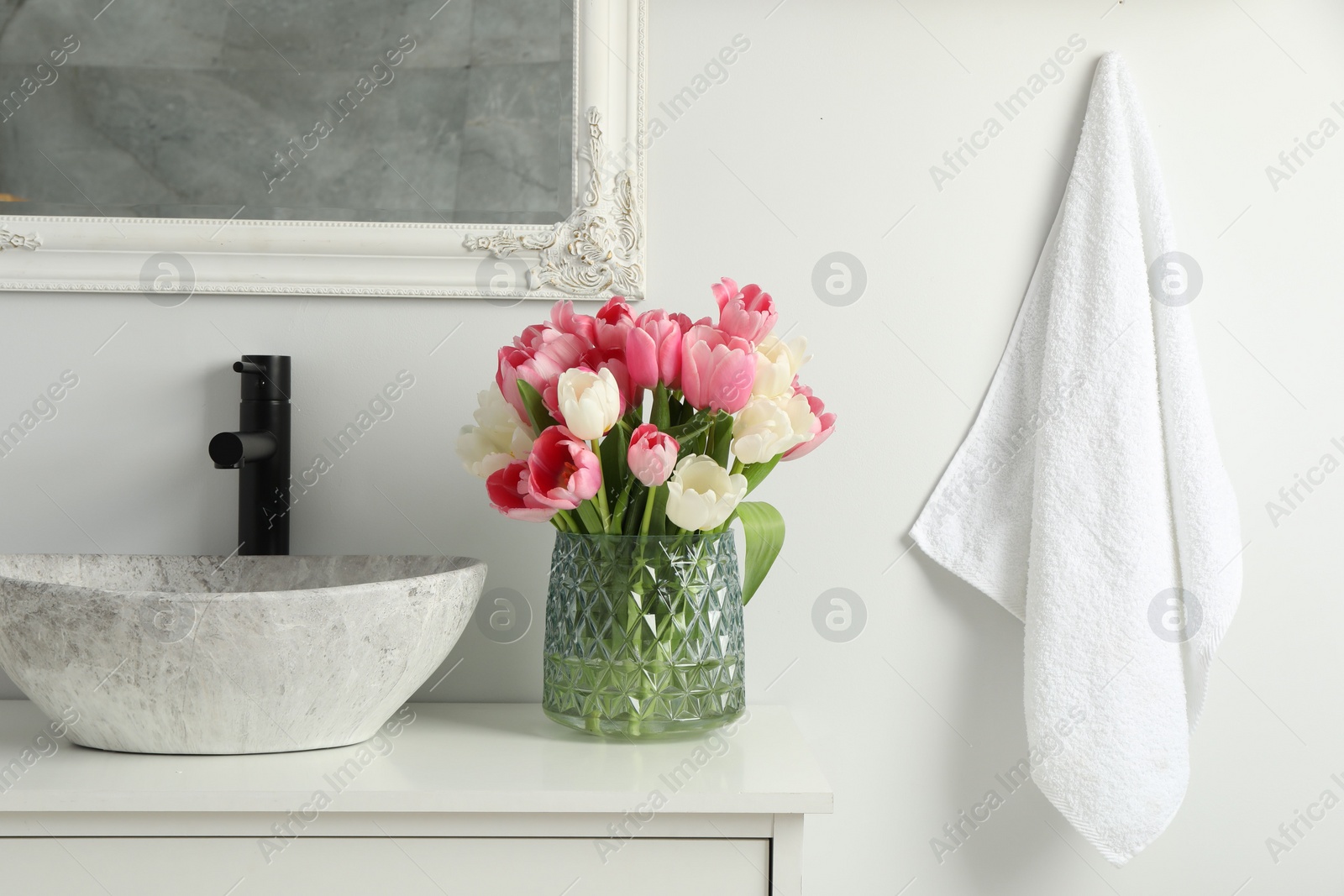 Photo of Vase with beautiful pink tulips and toiletries near sink in bathroom