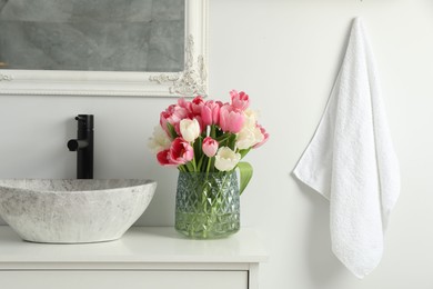 Vase with beautiful pink tulips and toiletries near sink in bathroom