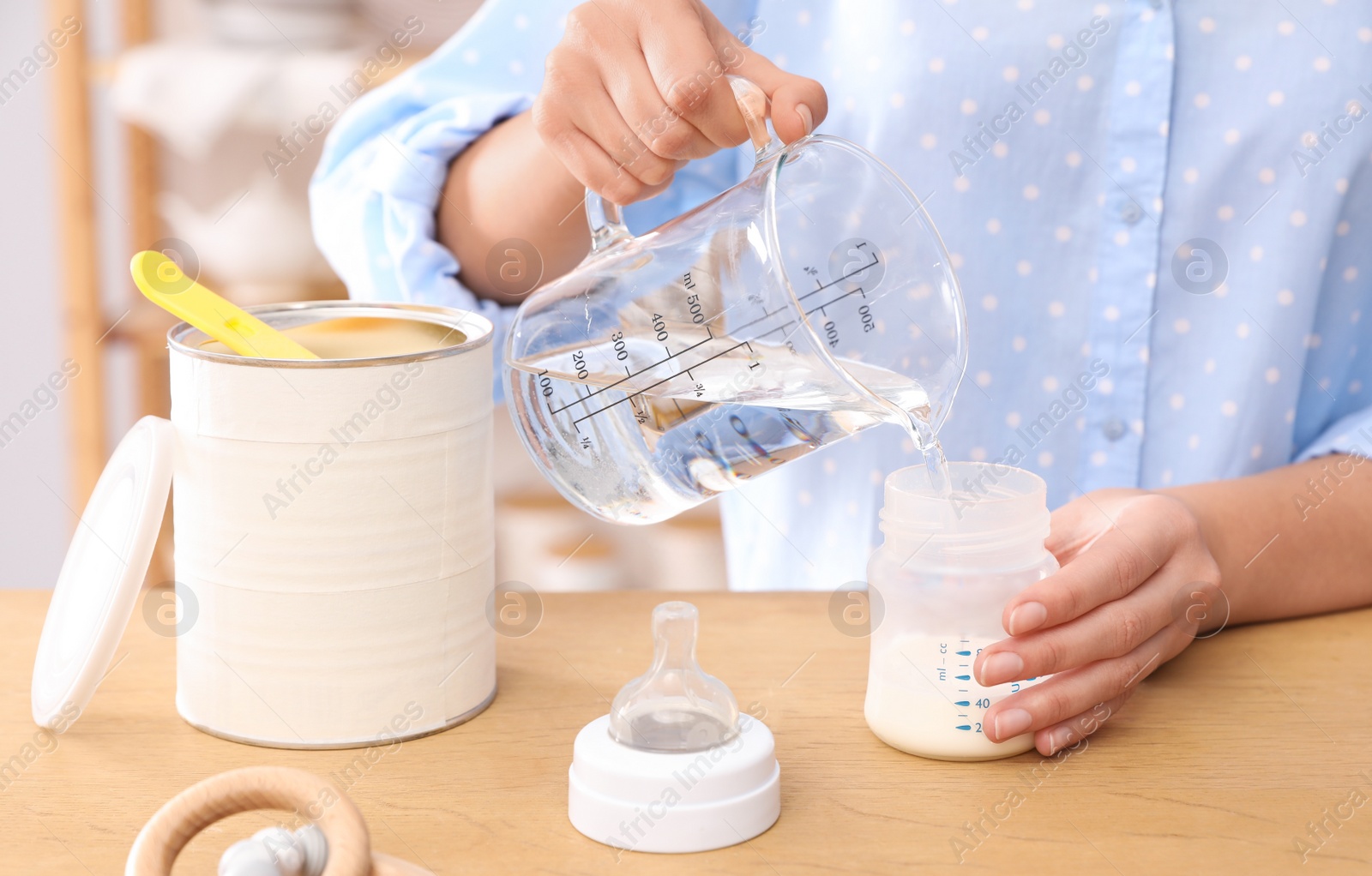 Photo of Woman preparing infant formula at table indoors, closeup. Baby milk