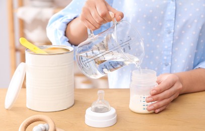 Photo of Woman preparing infant formula at table indoors, closeup. Baby milk