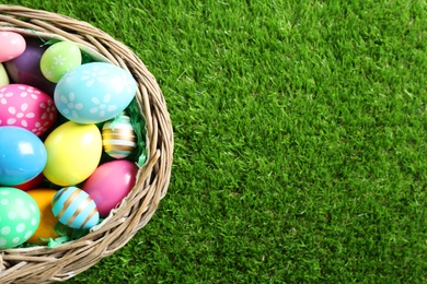 Photo of Wicker basket with Easter eggs on green grass, top view. Space for text