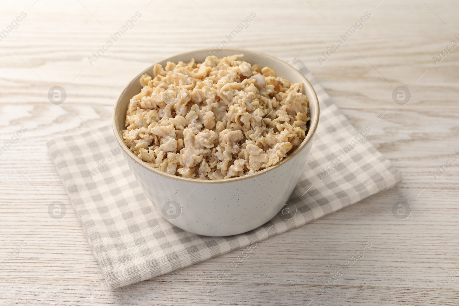 Photo of Tasty boiled oatmeal in bowl on light wooden table