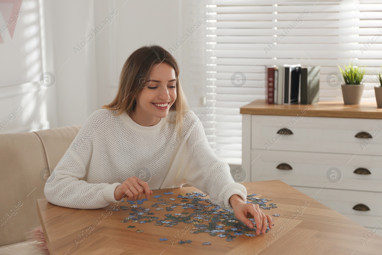 Photo of Happy woman playing with puzzles at wooden table indoors