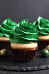Photo of Delicious cupcakes with green cream and Christmas decor on black table