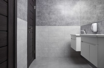 Photo of Public toilet interior with stylish white sinks, doors and tiles