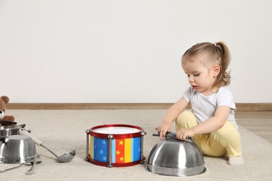 Cute little girl with cookware and toy drum at home