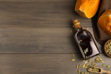 Photo of Glass bottle of oil with cut pumpkin and seeds on wooden table, flat lay. Space for text