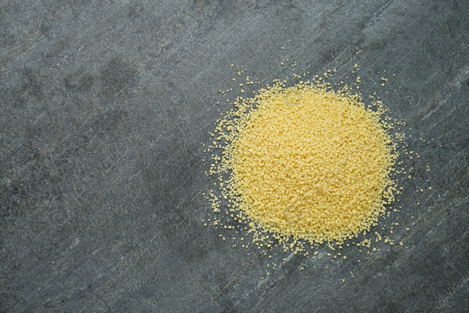 Photo of Heap of raw couscous on grey table, top view. Space for text