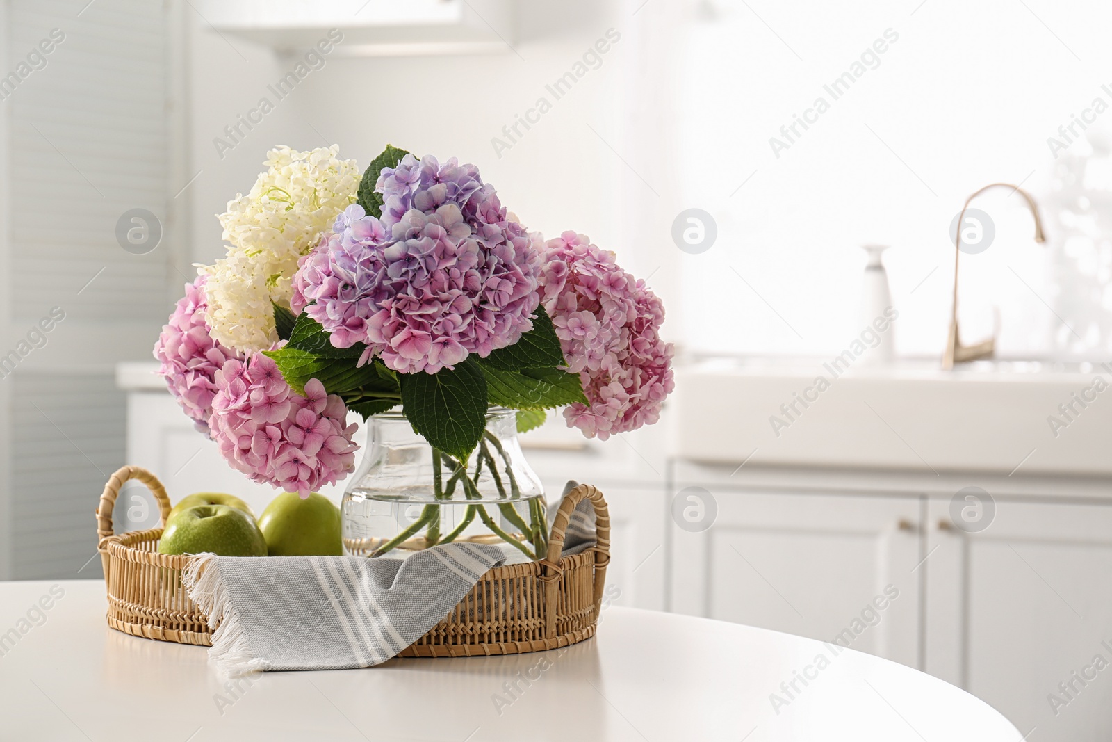 Photo of Bouquet of beautiful hydrangea flowers and apples on table in kitchen, space for text. Interior design