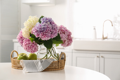 Photo of Bouquet of beautiful hydrangea flowers and apples on table in kitchen, space for text. Interior design