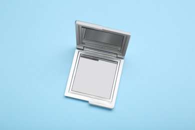 Photo of Stylish cosmetic pocket mirror on light blue background, top view