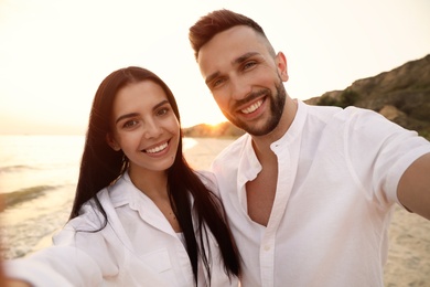 Photo of Happy young couple taking selfie on beach at sunset