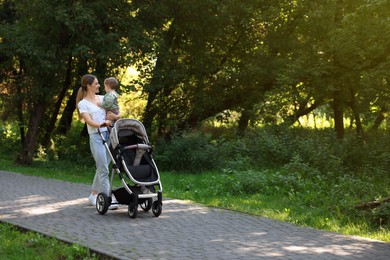 Photo of Happy nanny with cute little boy and stroller walking in park, space for text