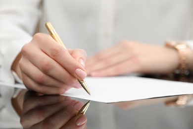 Photo of Woman writing on sheet of paper at glass table, closeup