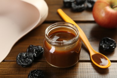 Tasty baby food in jar, spoon and dried prunes on wooden table, closeup