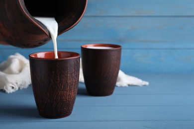 Photo of Pouring milk into clay cup on light blue wooden table, space for text