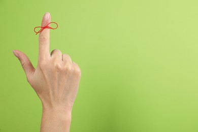 Photo of Woman showing index finger with tied red bow as reminder on light green background, closeup. Space for text