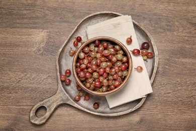 Bowl of fresh ripe gooseberries on wooden table, flat lay. Space for text