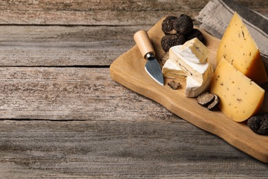Photo of Different types of cheese, knife and truffles on wooden table, space for text