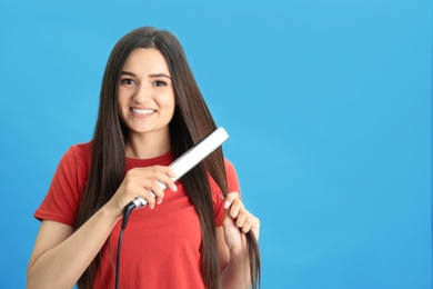 Photo of Young woman using hair iron on blue background, space for text