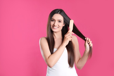 Beautiful smiling young woman with hair brush on color background