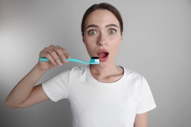 Photo of Surprised woman holding brush with charcoal toothpaste on grey background