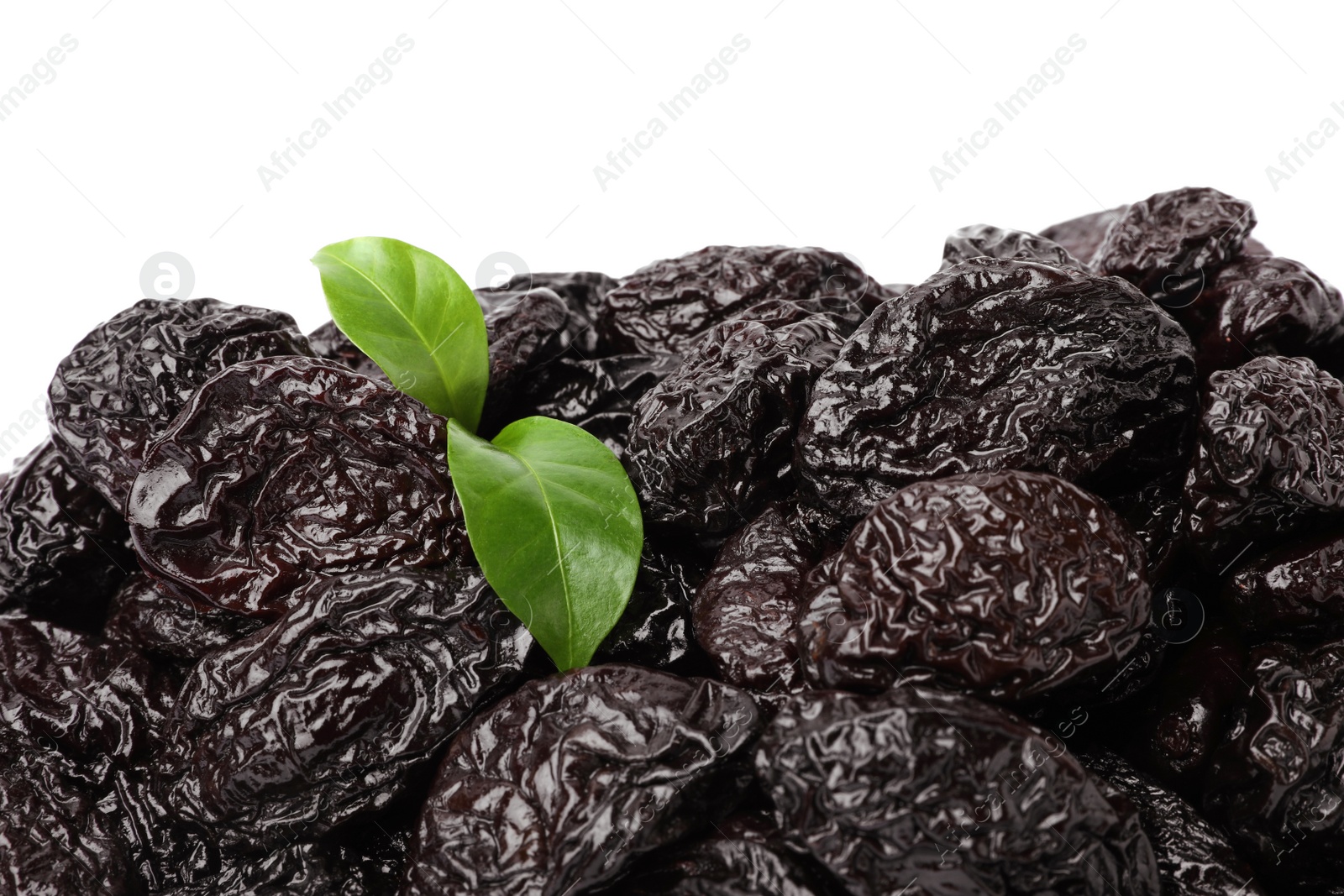 Photo of Pile of sweet dried prunes and green leaves on white background, closeup