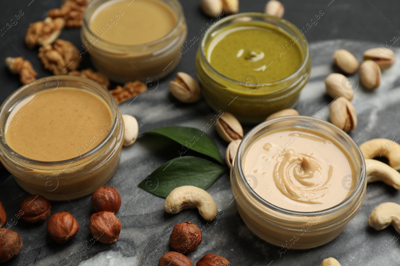 Photo of Jars with butters made of different nuts and ingredients on black table, closeup