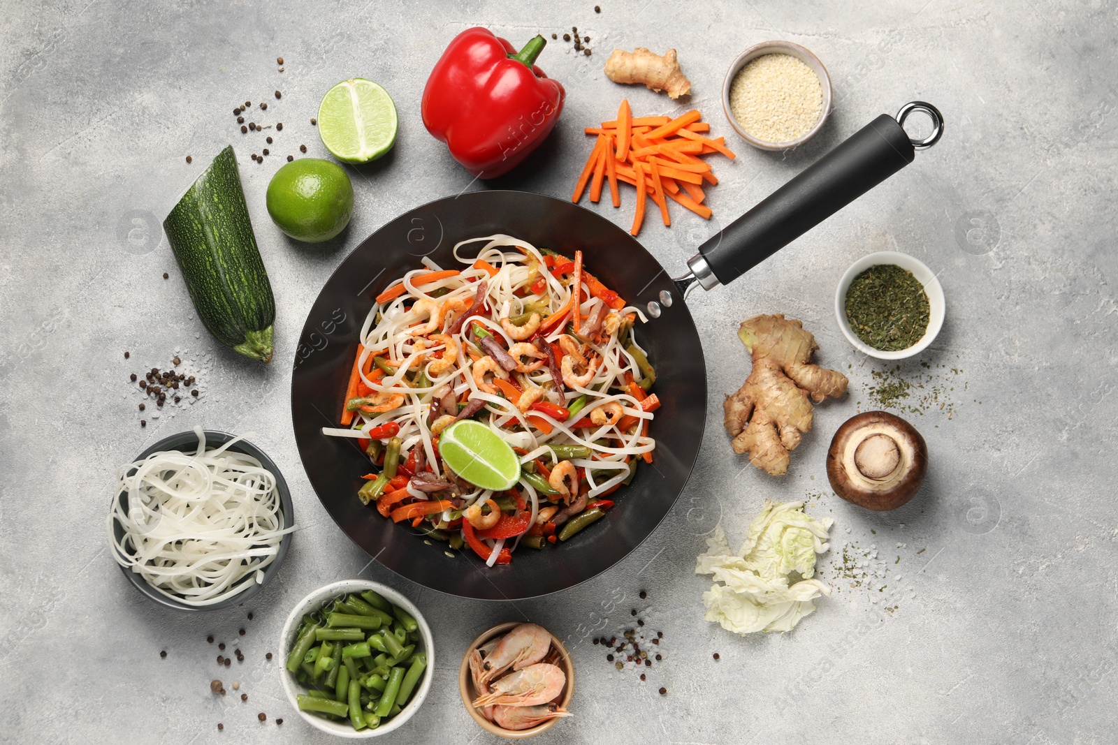 Photo of Shrimp stir fry with noodles and vegetables in wok surrounded by ingredients on grey table, flat lay