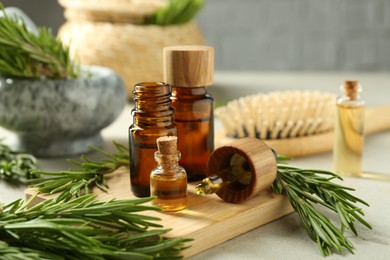 Photo of Essential oils in bottles and rosemary on light gray table, closeup