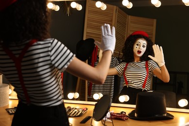 Photo of Young woman in mime costume posing near mirror indoors