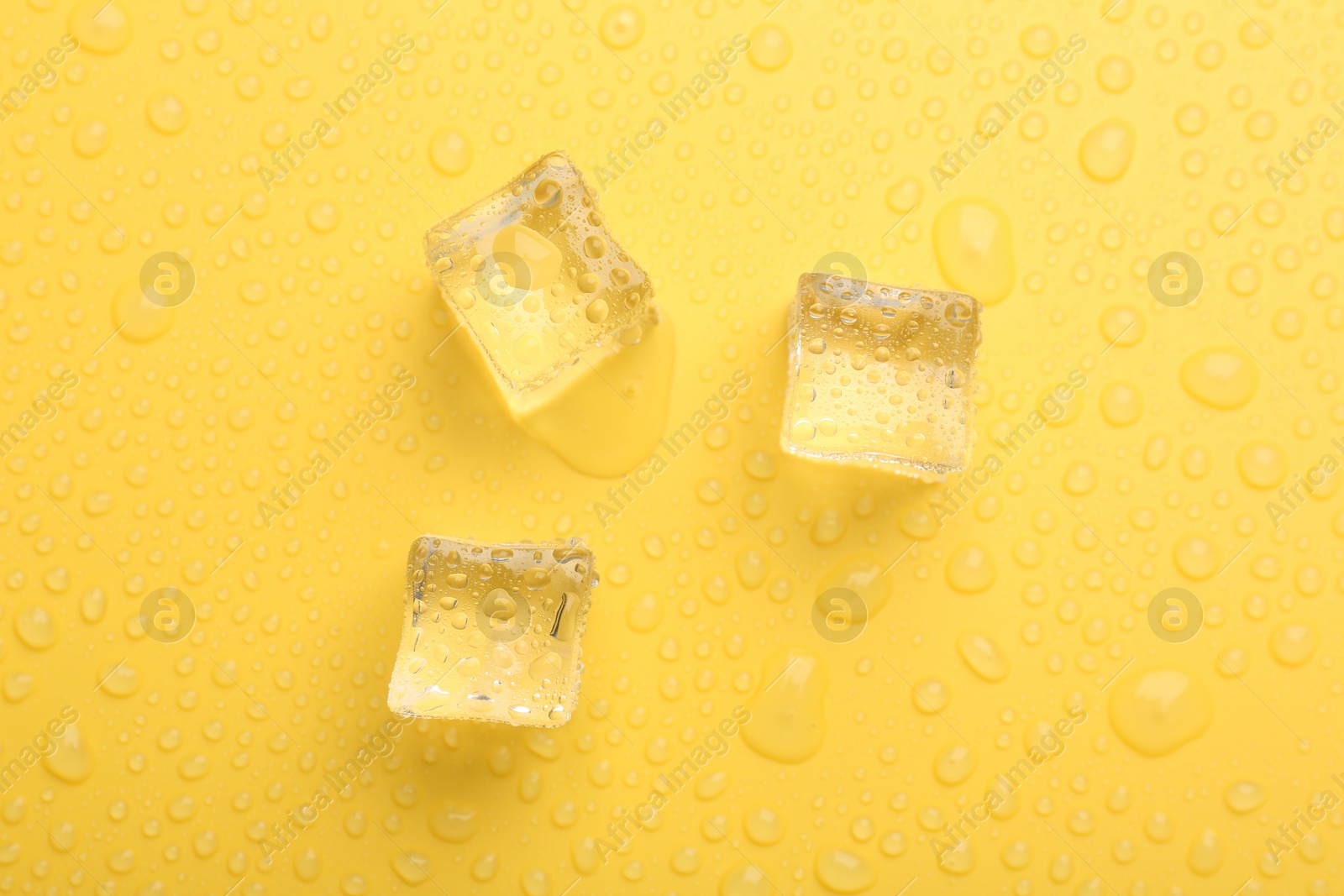 Photo of Crystal clear ice cubes on yellow background, flat lay