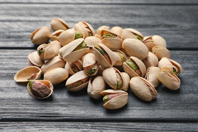 Photo of Heap of organic pistachio nuts on wooden table, closeup