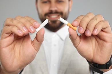 Photo of Stop smoking concept. Man breaking cigarette on light grey background, selective focus