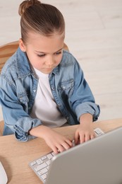 Photo of Little girl using laptop at table indoors. Internet addiction