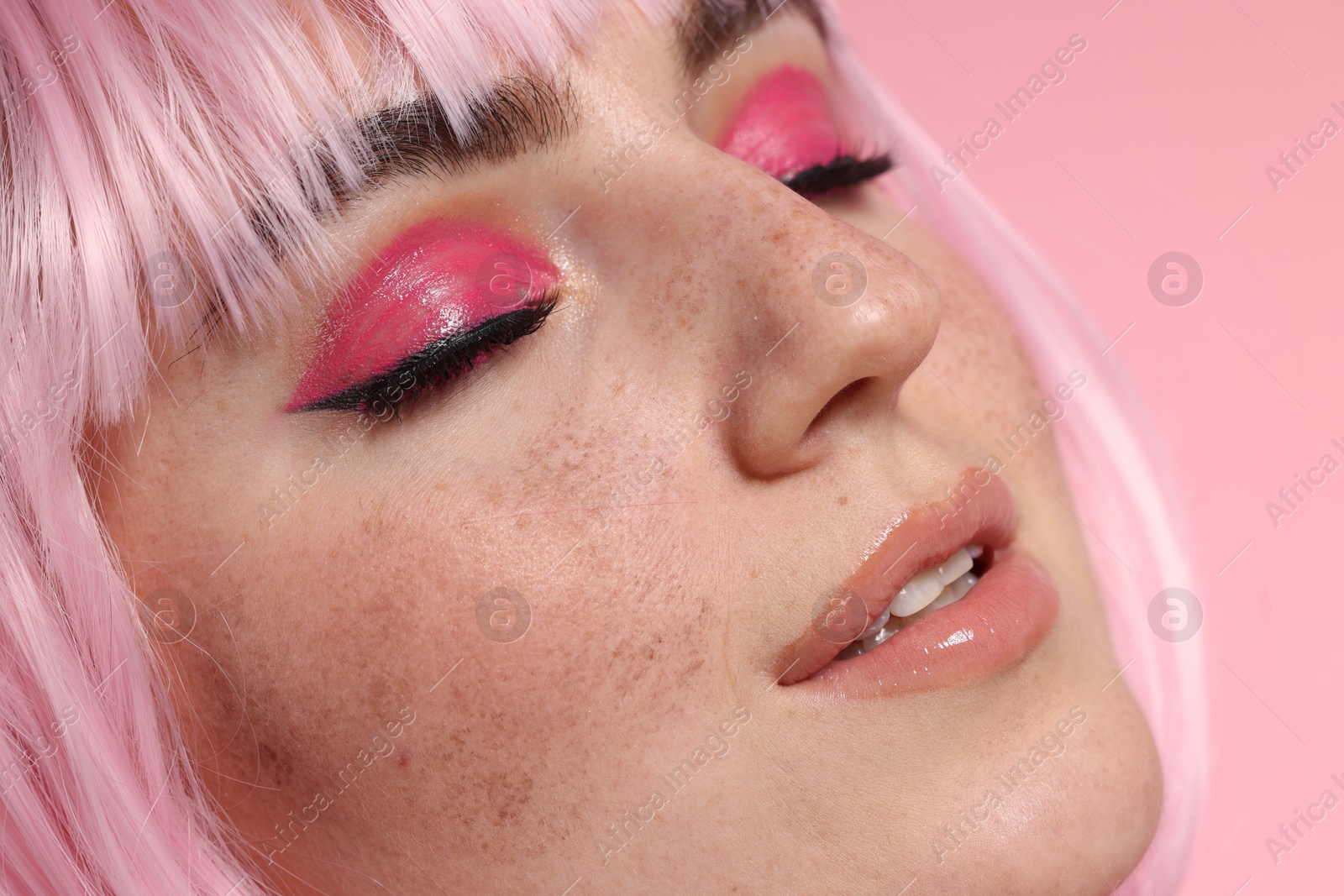 Photo of Beautiful woman with bright makeup and fake freckles on pink background, closeup