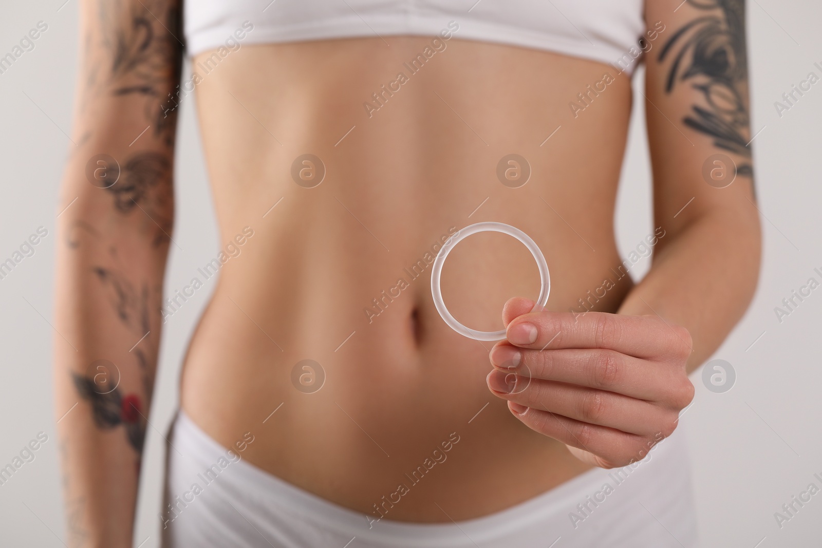 Photo of Woman holding contraceptive diaphragm (vaginal ring) on light grey background, closeup