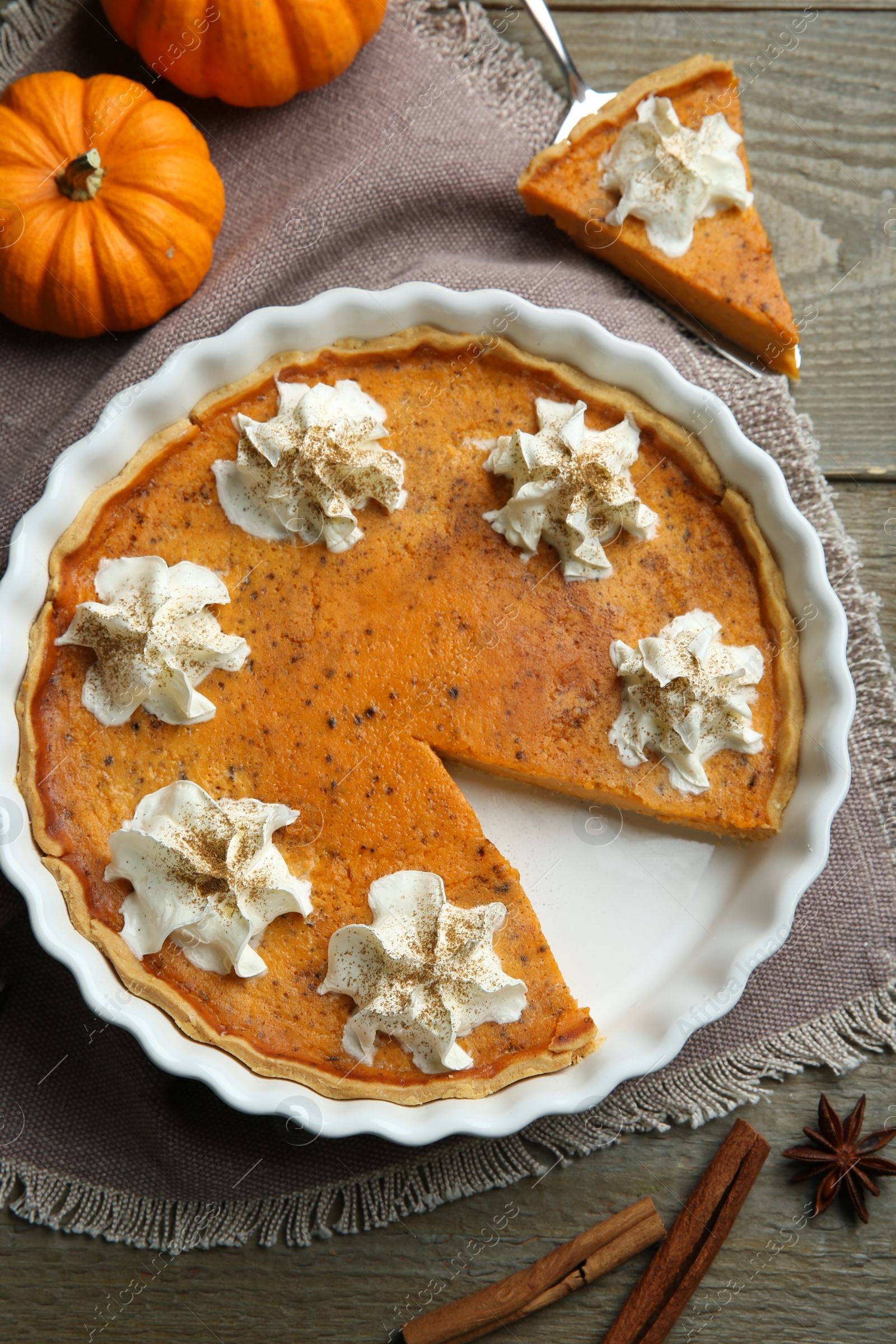 Photo of Delicious pumpkin pie with whipped cream and spices on wooden table, flat lay