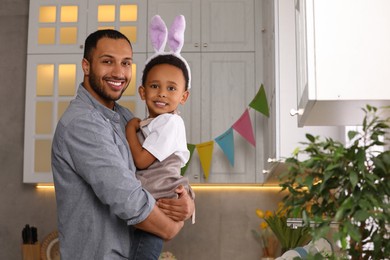 Photo of Happy African American father and his cute son in bunny ears headband in kitchen. Easter celebration
