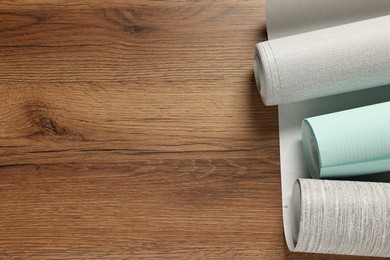 Photo of Different wallpaper rolls on wooden table, flat lay. Space for text