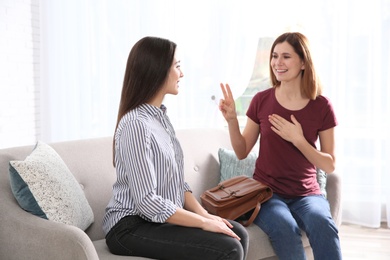 Photo of Hearing impaired friends using sign language for communication on sofa in living room