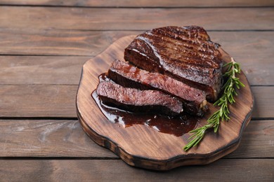 Photo of Delicious grilled beef meat and rosemary on wooden table, closeup. Space for text
