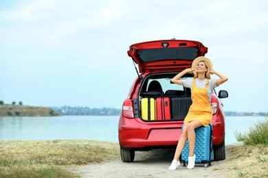 Photo of Happy woman near car trunk with suitcases on riverside. Space for text
