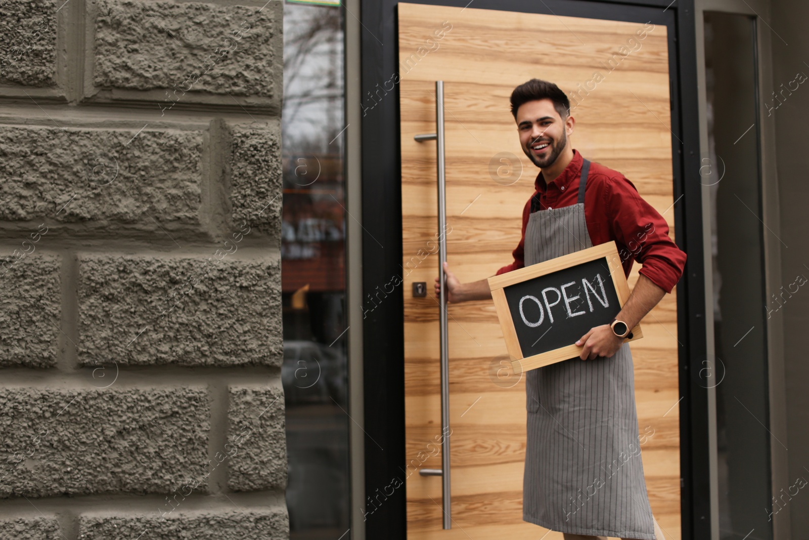 Photo of Young male business owner holding OPEN sign near his cafe. Space for text