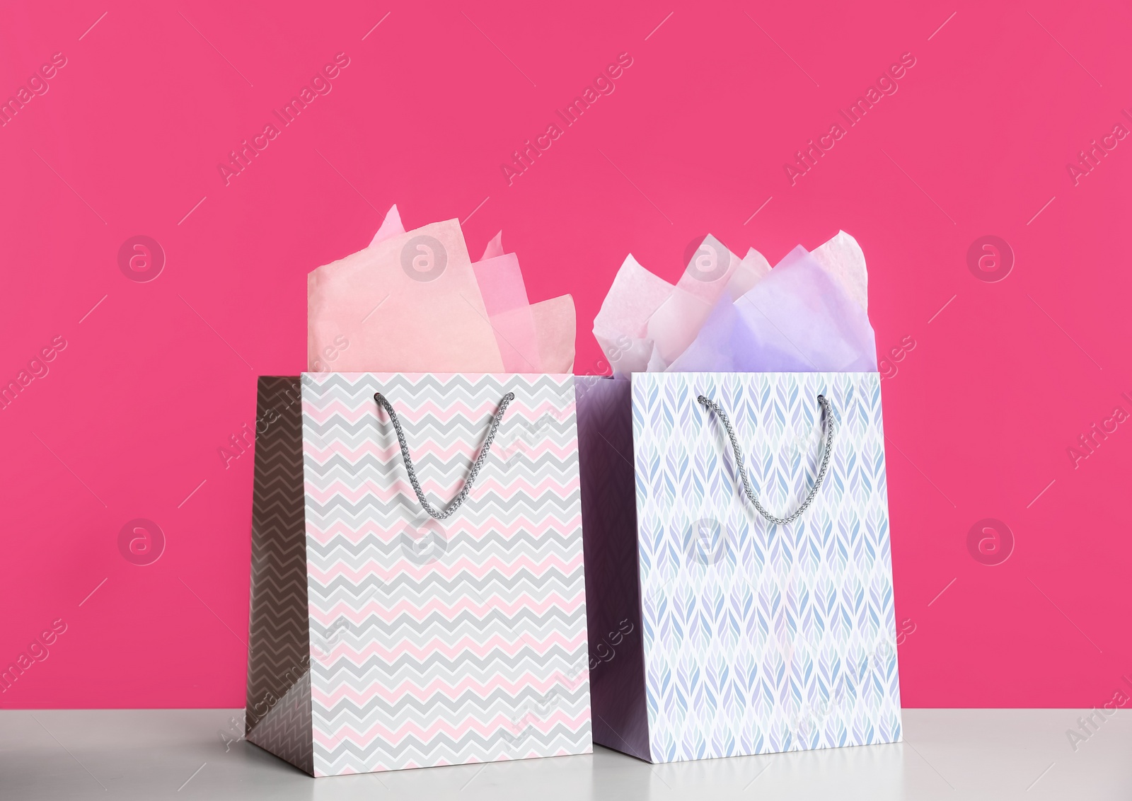 Photo of Gift bags with paper on white table against pink background