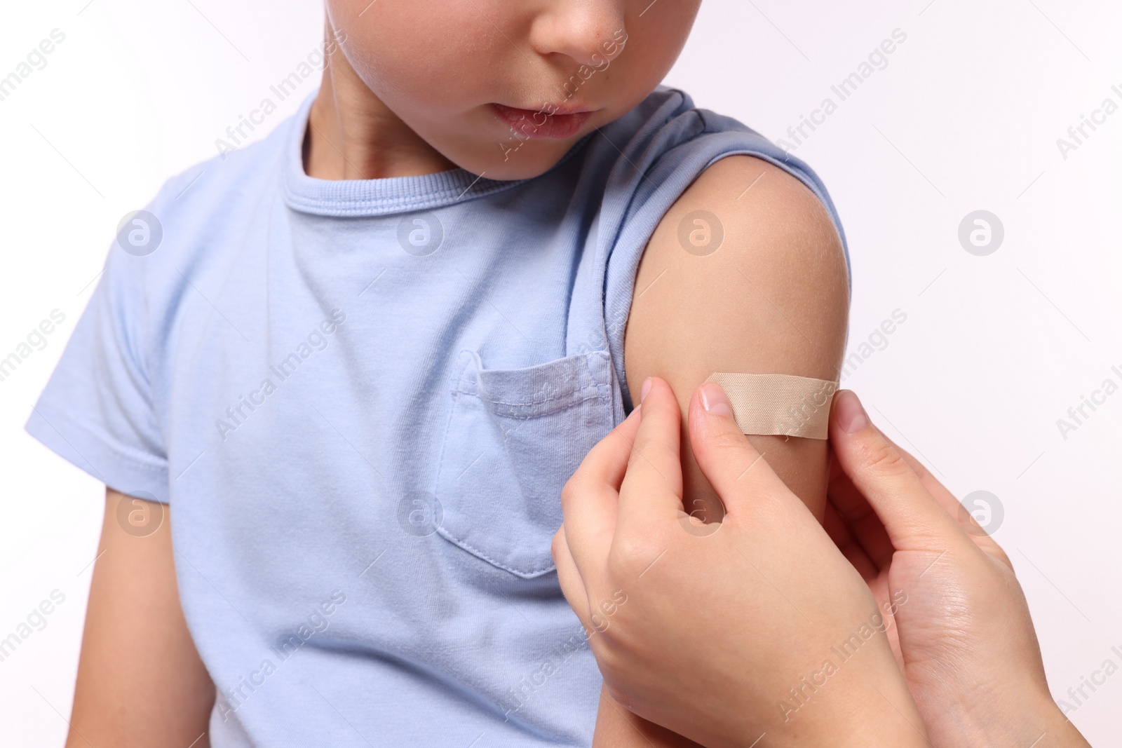 Photo of Woman sticking plaster on boy's arm after vaccination against white background, closeup