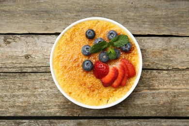 Photo of Delicious creme brulee with berries and mint in bowl on wooden table, top view